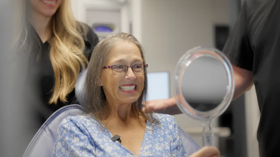 Patient smiling at her new teeth in a hand mirror